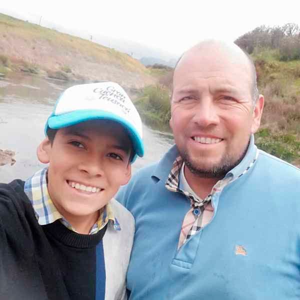 Un hombre y un niño posan para una fotografía junto a un río.