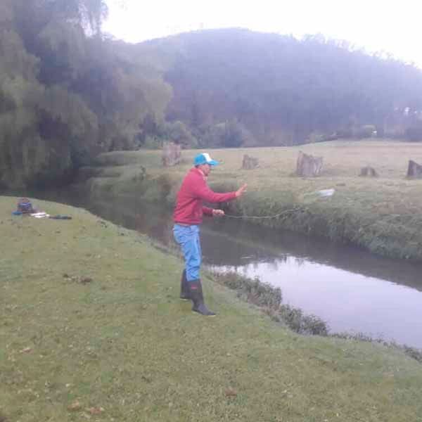 Un hombre con una chaqueta roja y pantalones azules está pescando en un río.