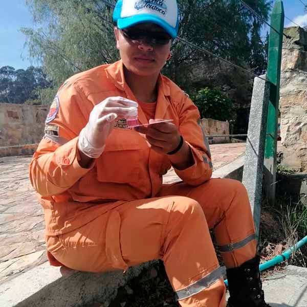 Un hombre con un mono naranja y un sombrero azul está sentado en una acera mirando su teléfono celular.