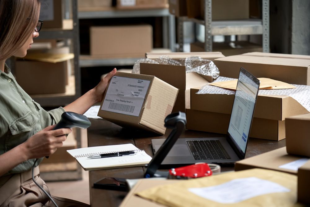 A woman is using a scanner to scan a box in a warehouse.