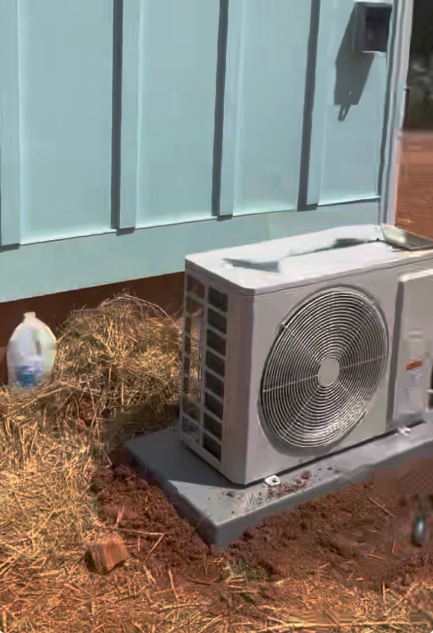 An outdoor air conditioning unit sits on a concrete pad next to a light blue wall.