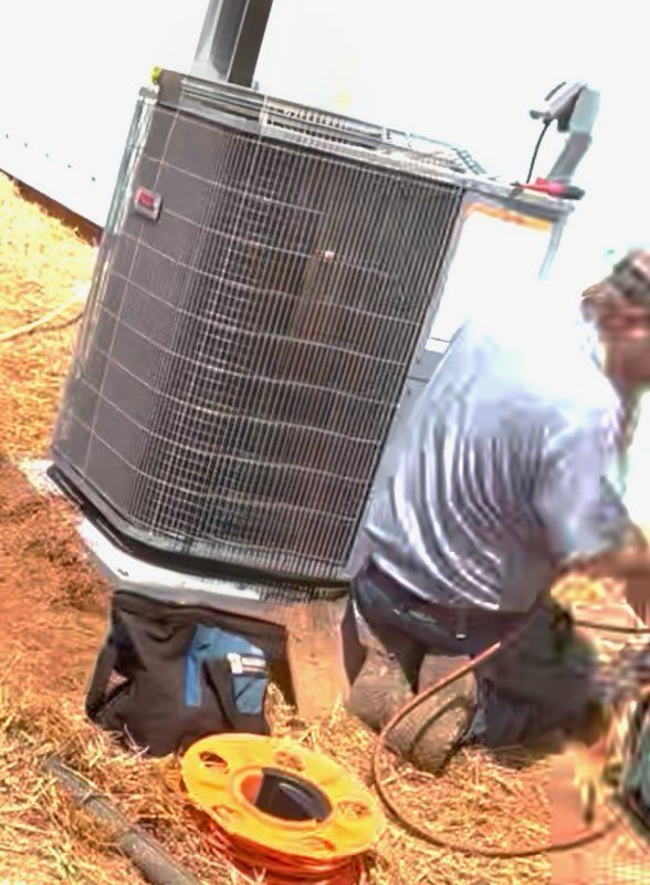 A technician kneeling on the ground, performing maintenance on an outdoor residential air conditioning unit.