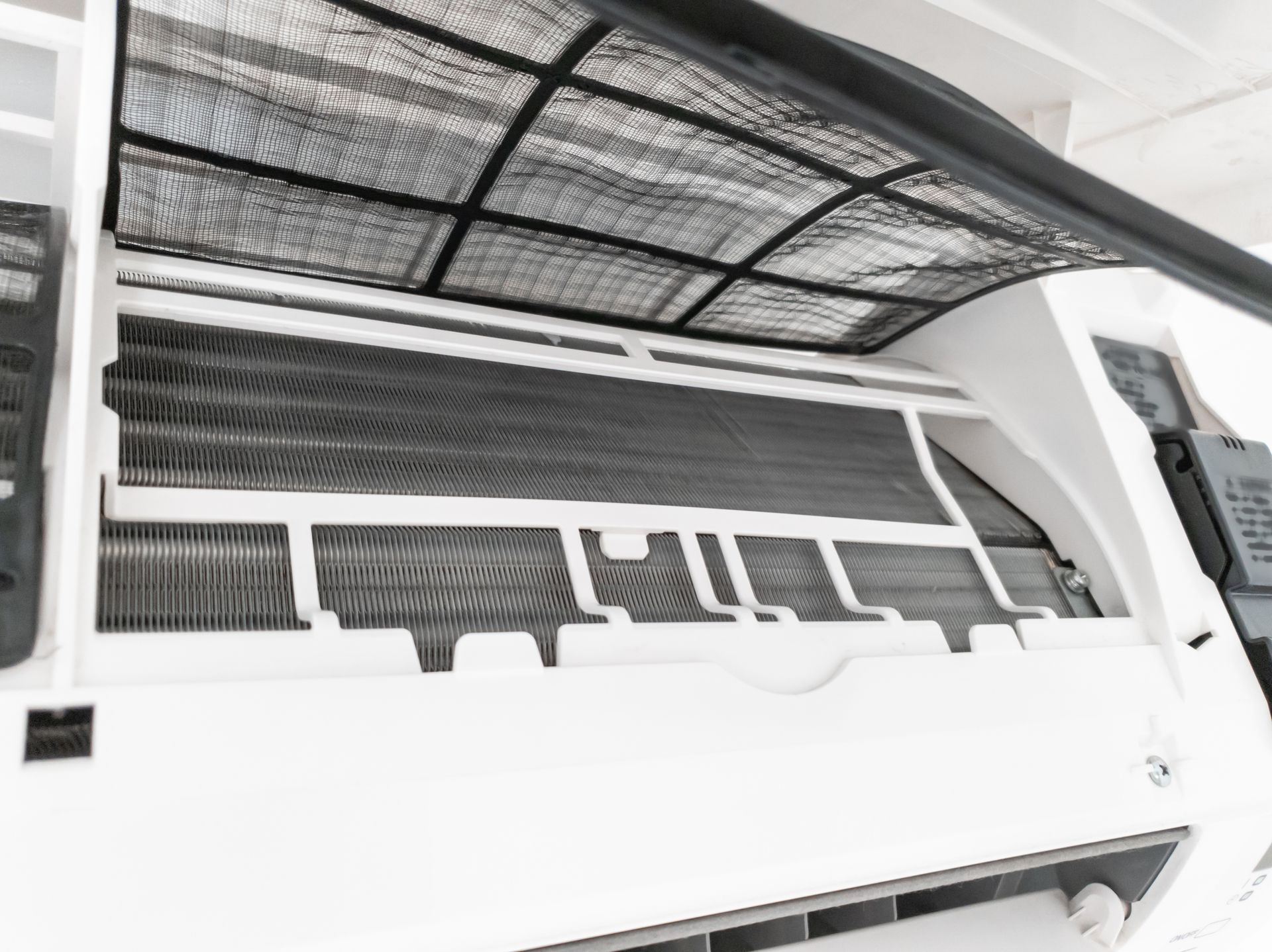 A white split-system air conditioner unit with its front panel open, revealing the internal dust filter and cooling coils.