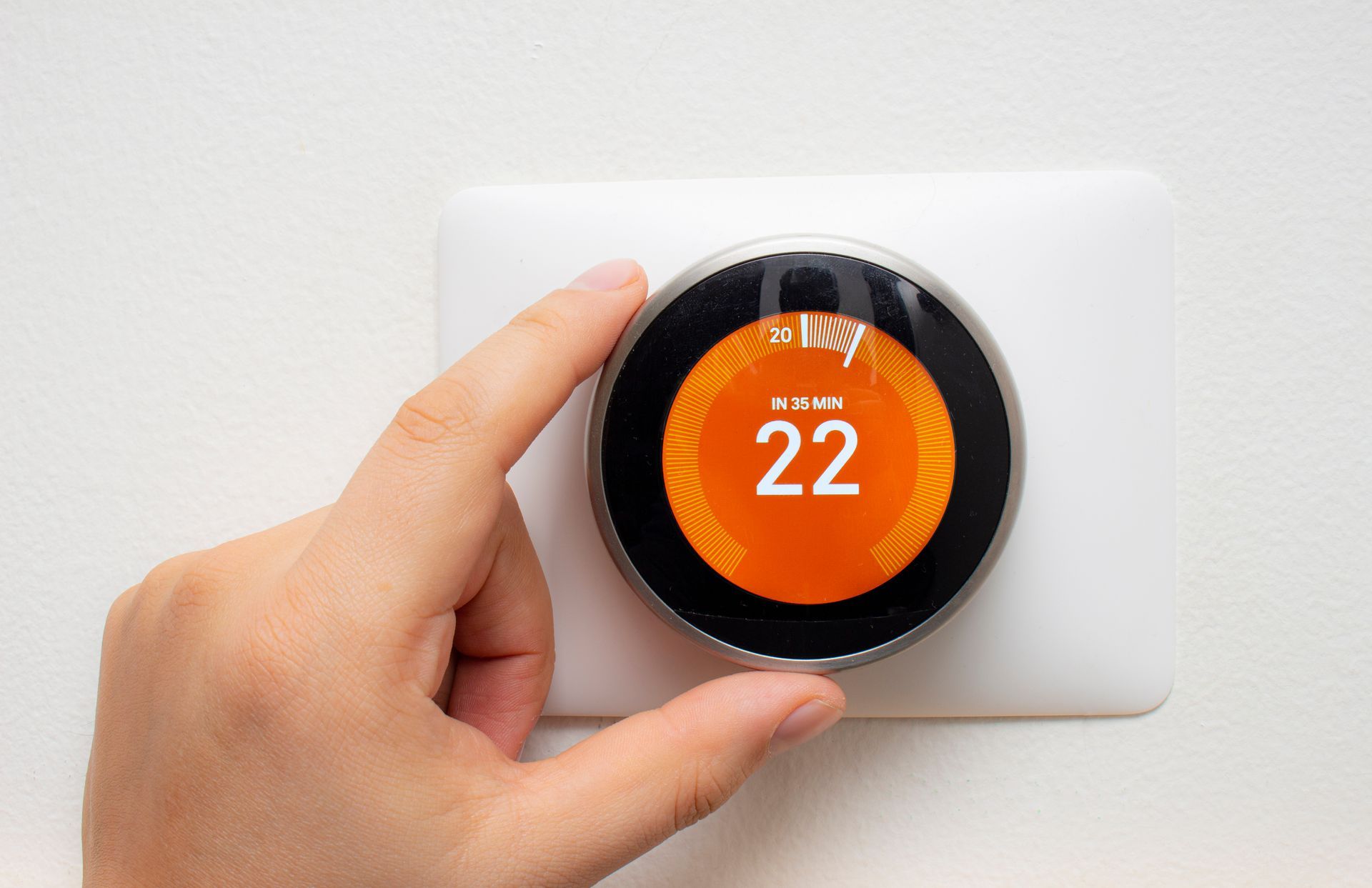A hand adjusts a Nest smart thermostat.