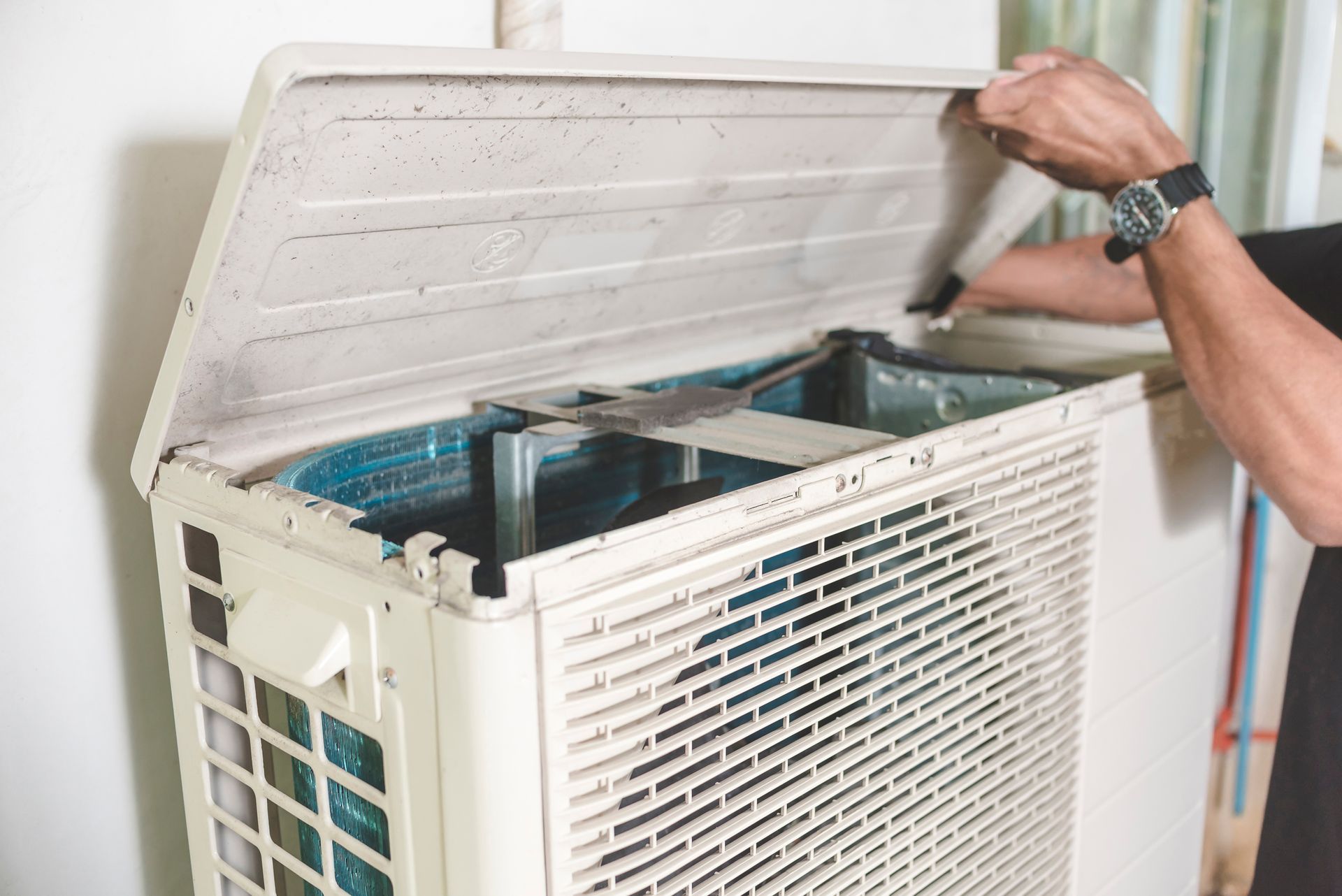 A person wearing a watch opens the top panel of an outdoor air conditioning unit to perform maintenance.