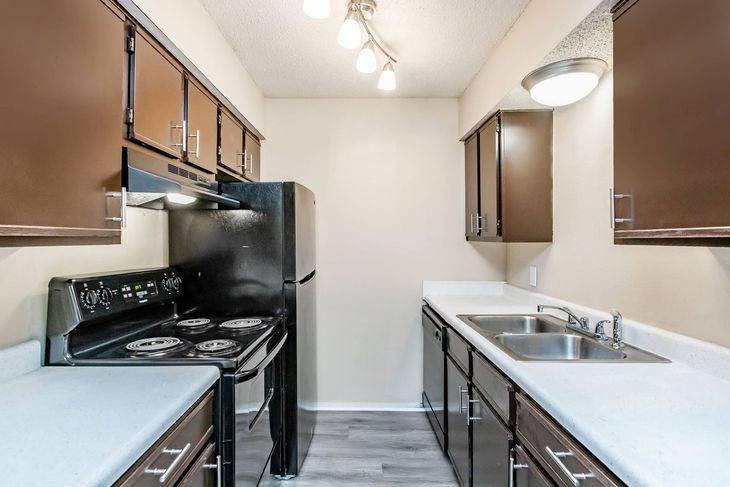 Small galley kitchen with black appliances, brown cabinets, and white countertops.
