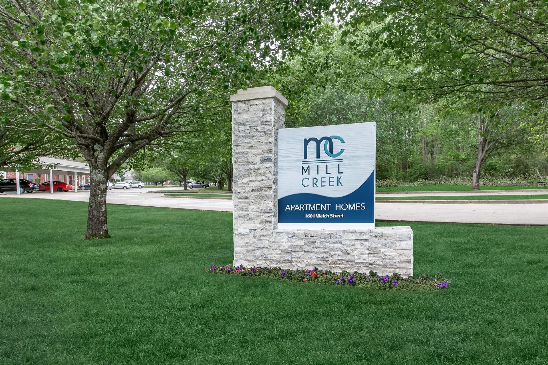 Sign for Mill Creek apartment homes, blue and white on gray stone, on green lawn.