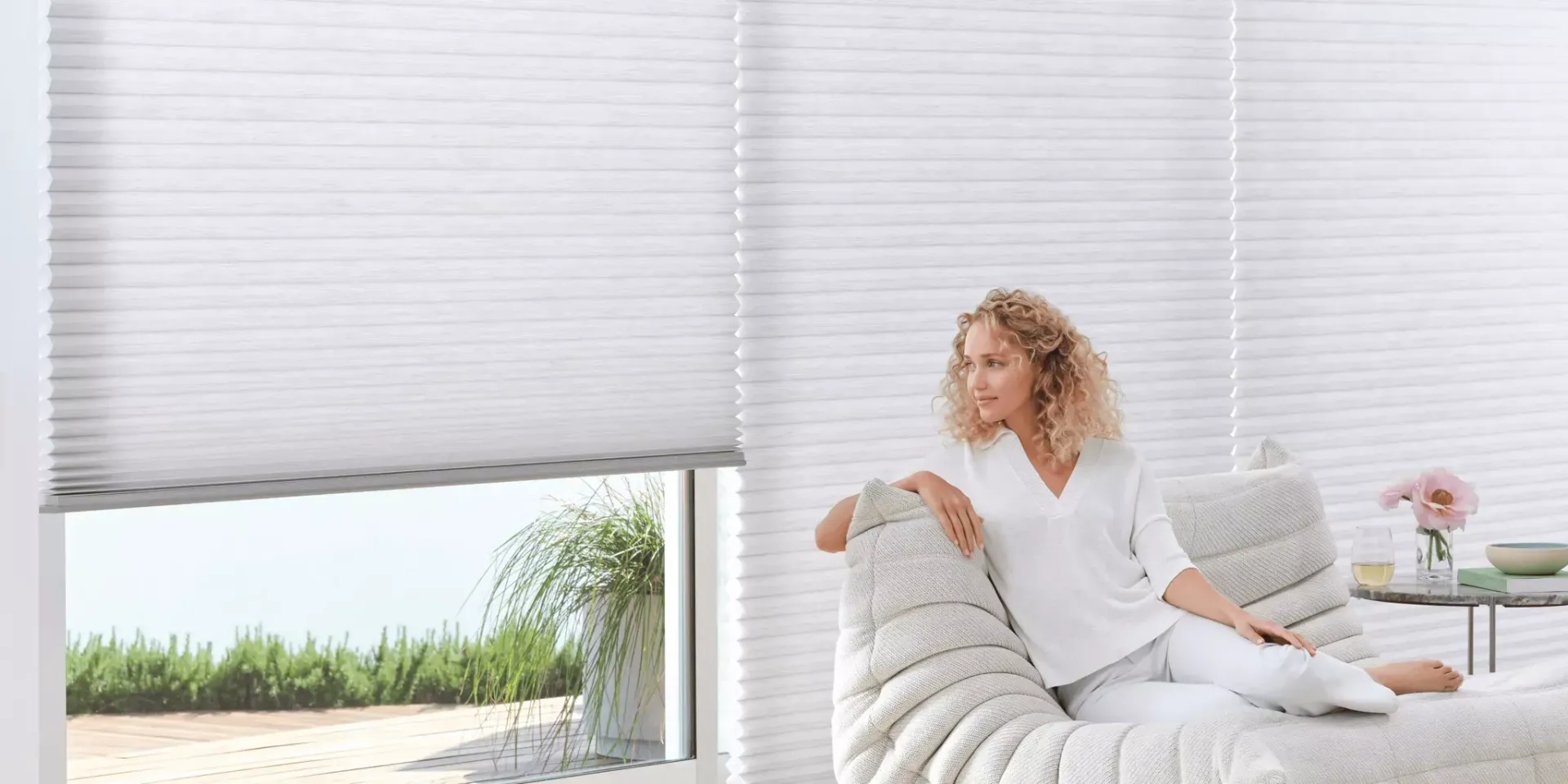 A woman is sitting on a couch in front of a window with blinds.
