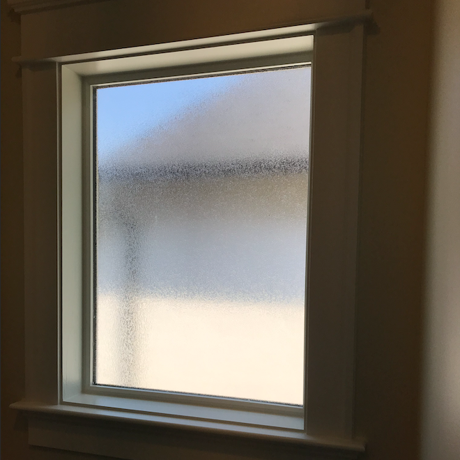 A square window with a white frame and frosted glass in a room.
