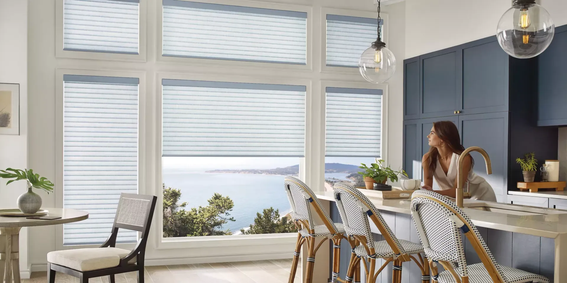 A woman is sitting at a counter in a kitchen looking out the window.