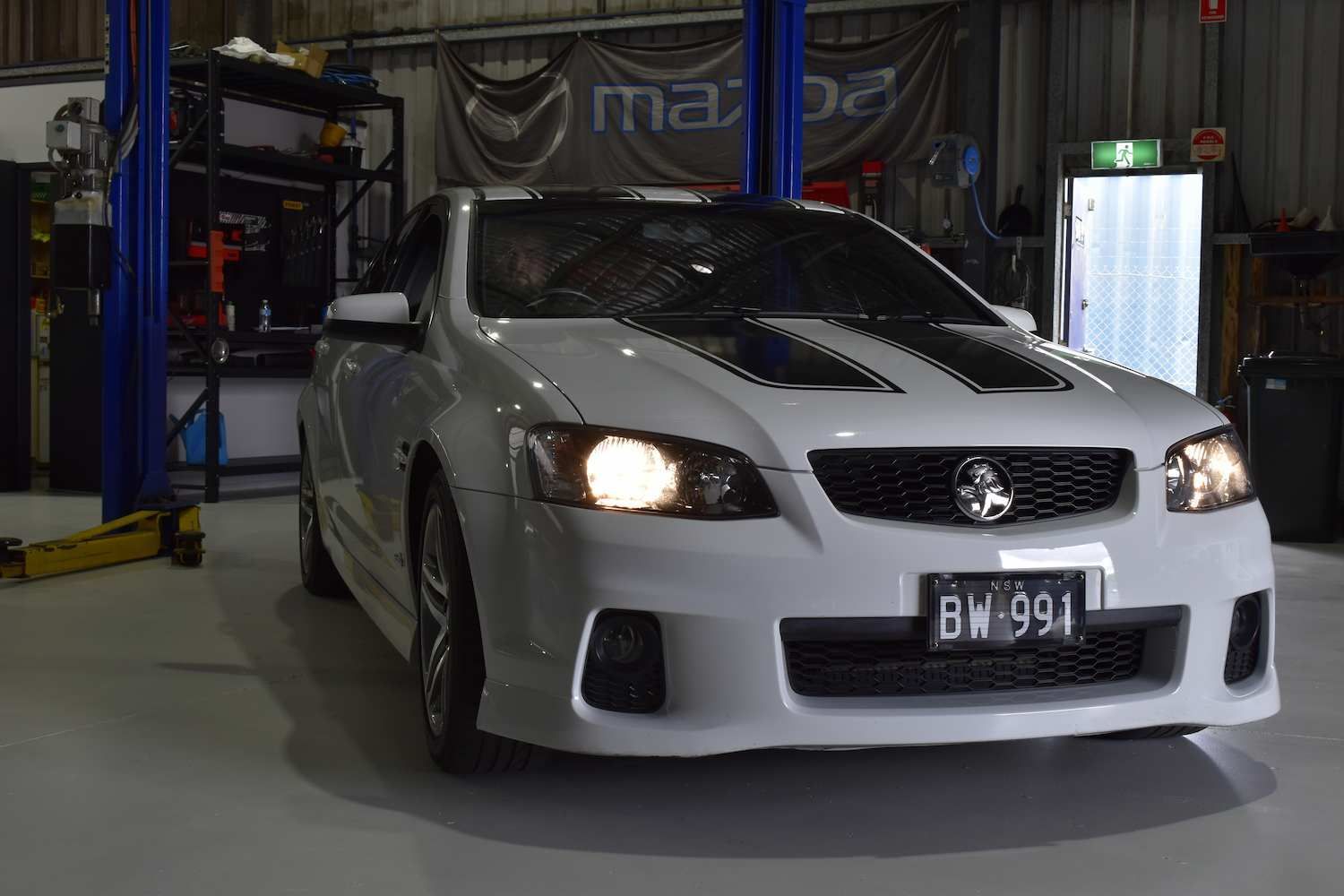 A White Car is Parked in a Garage on a Lift — Optimum Automotive & Road Service In Huskisson, NSW