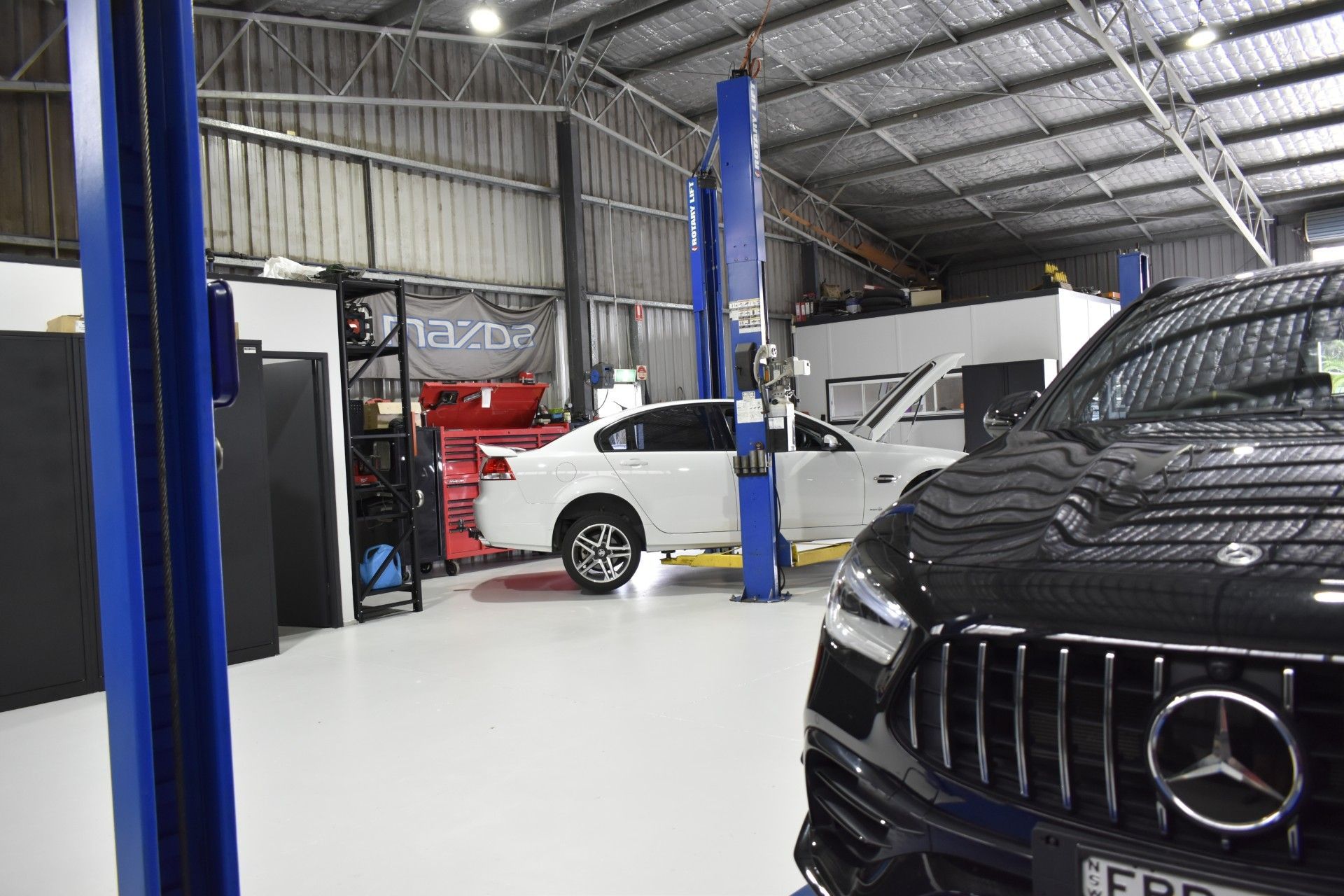 A Man is Working on a Car on a Lift in a Garage — Optimum Automotive & Road Service in Jervis Bay, NSW