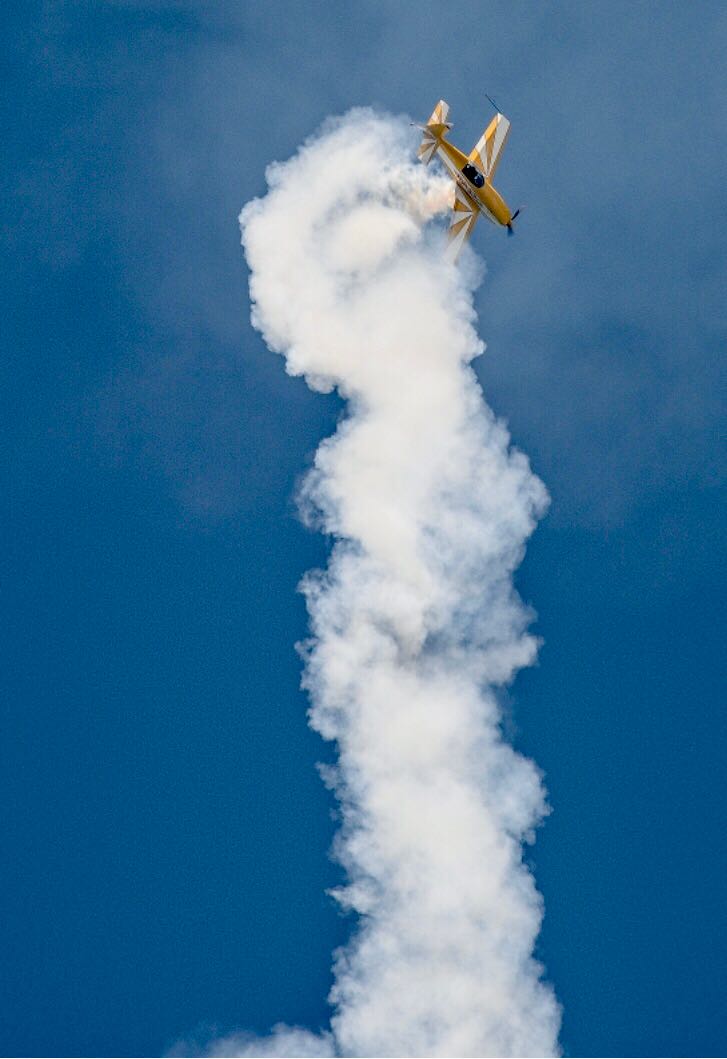 A yellow airplane is flying through a blue sky with smoke coming out of it