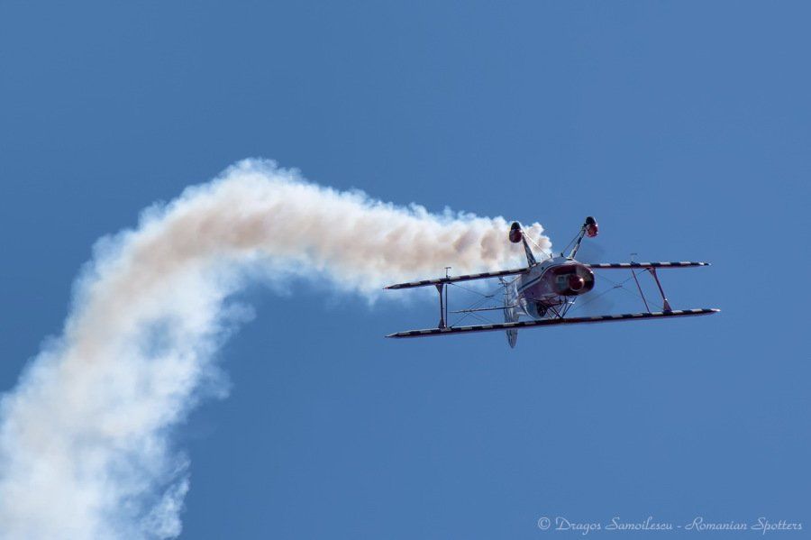 A biplane is flying through a blue sky with smoke coming out of it.