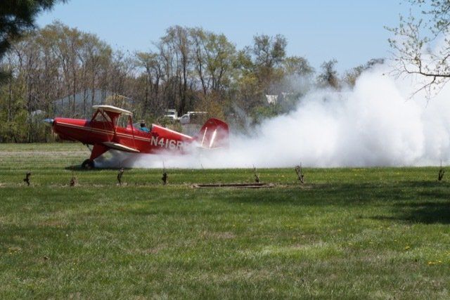 A small red airplane is taking off from a grassy field.