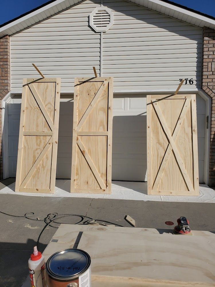 Three wooden barn doors are being built in front of a house.