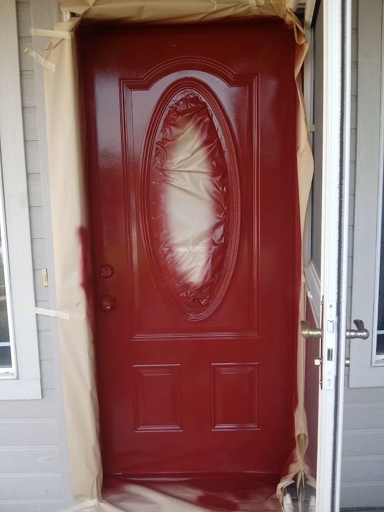 A red door with an oval window is being painted.