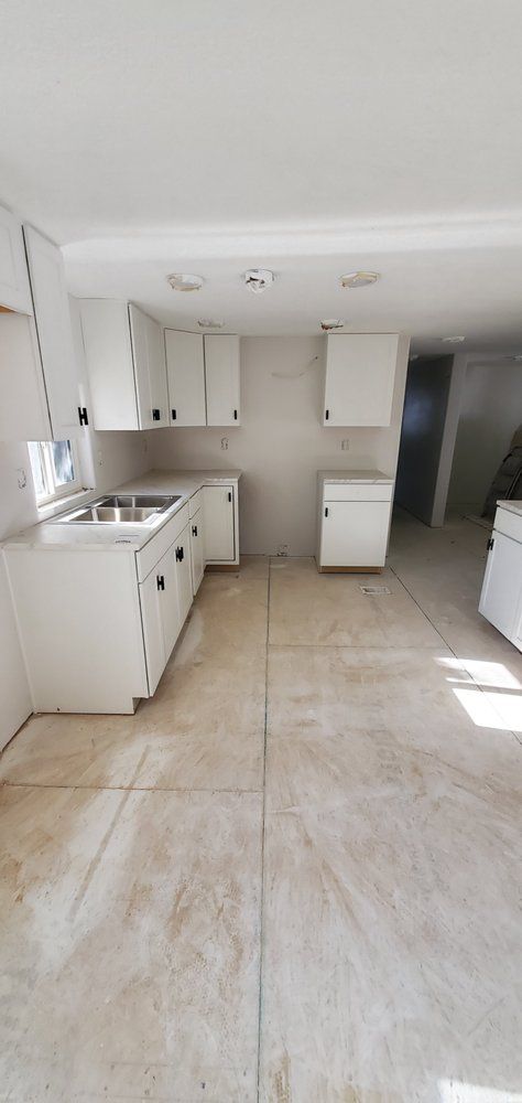 An empty kitchen with white cabinets and a sink.