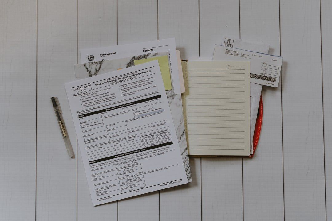 A pile of papers and notebooks on a wooden table.