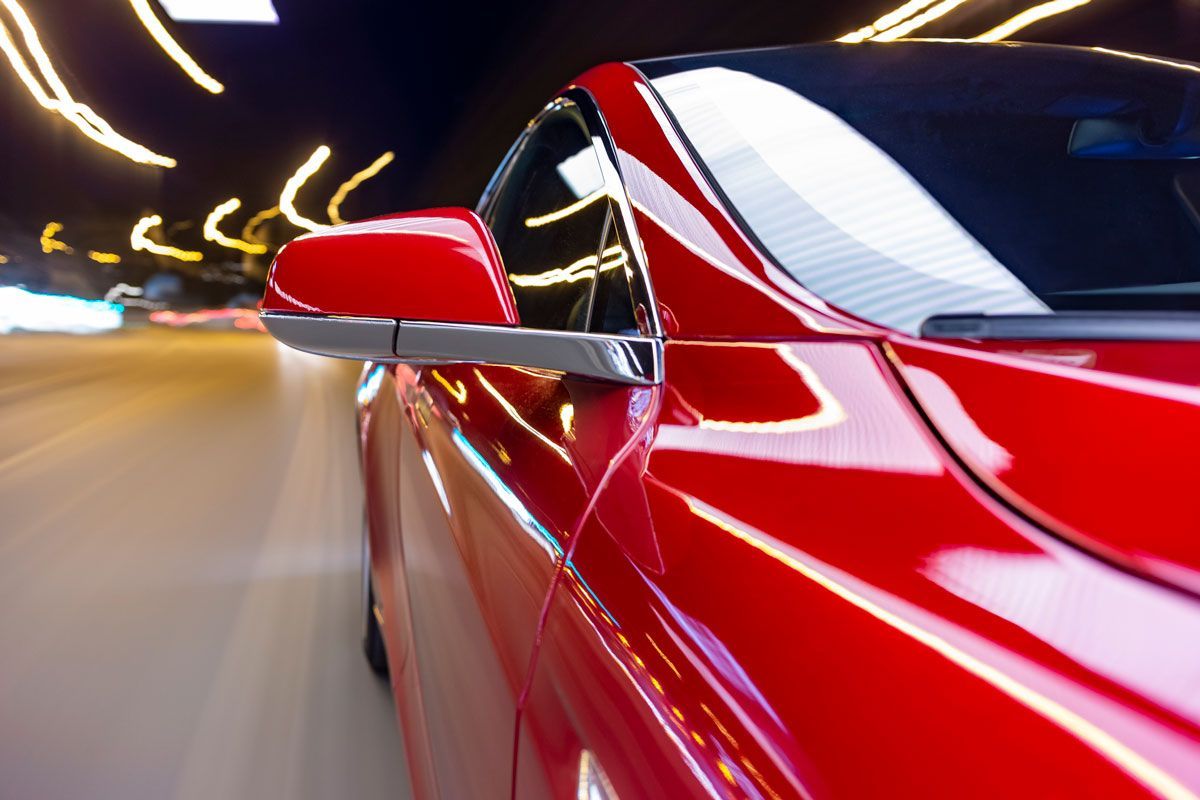 Red car speeding down a road at night, blurred lights in the background.