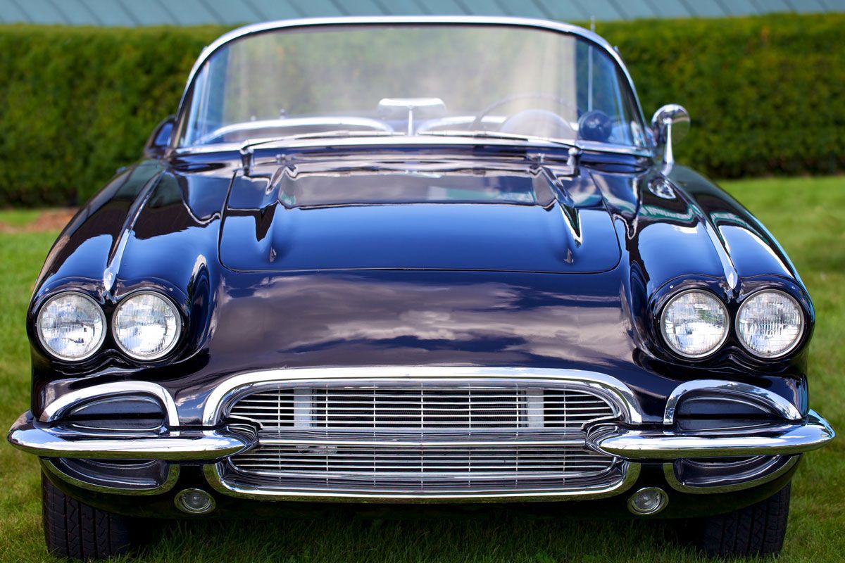 Dark blue vintage convertible car, parked on grass, with a chrome grill and headlights.