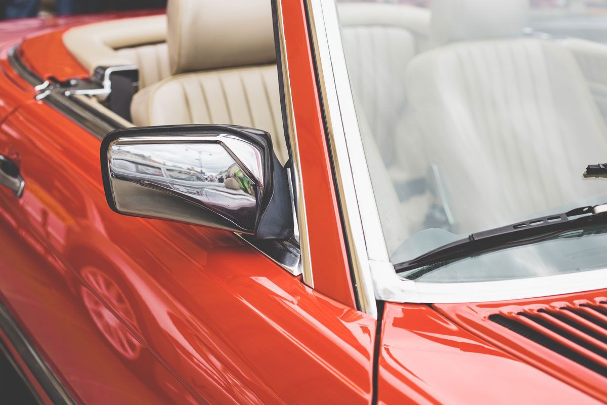 Red convertible car with beige interior, chrome mirror, and windshield.