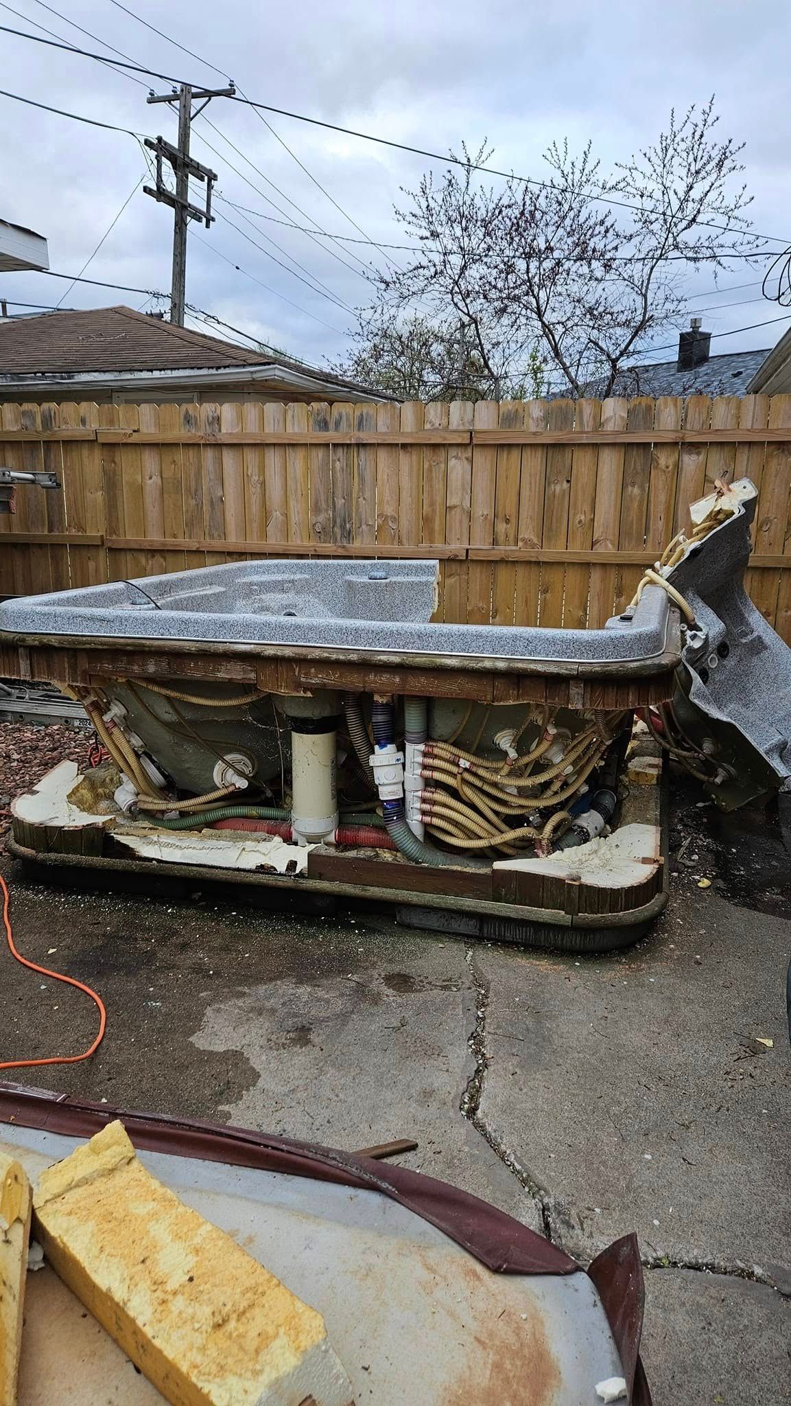 A hot tub is sitting on the ground in a backyard next to a wooden fence.