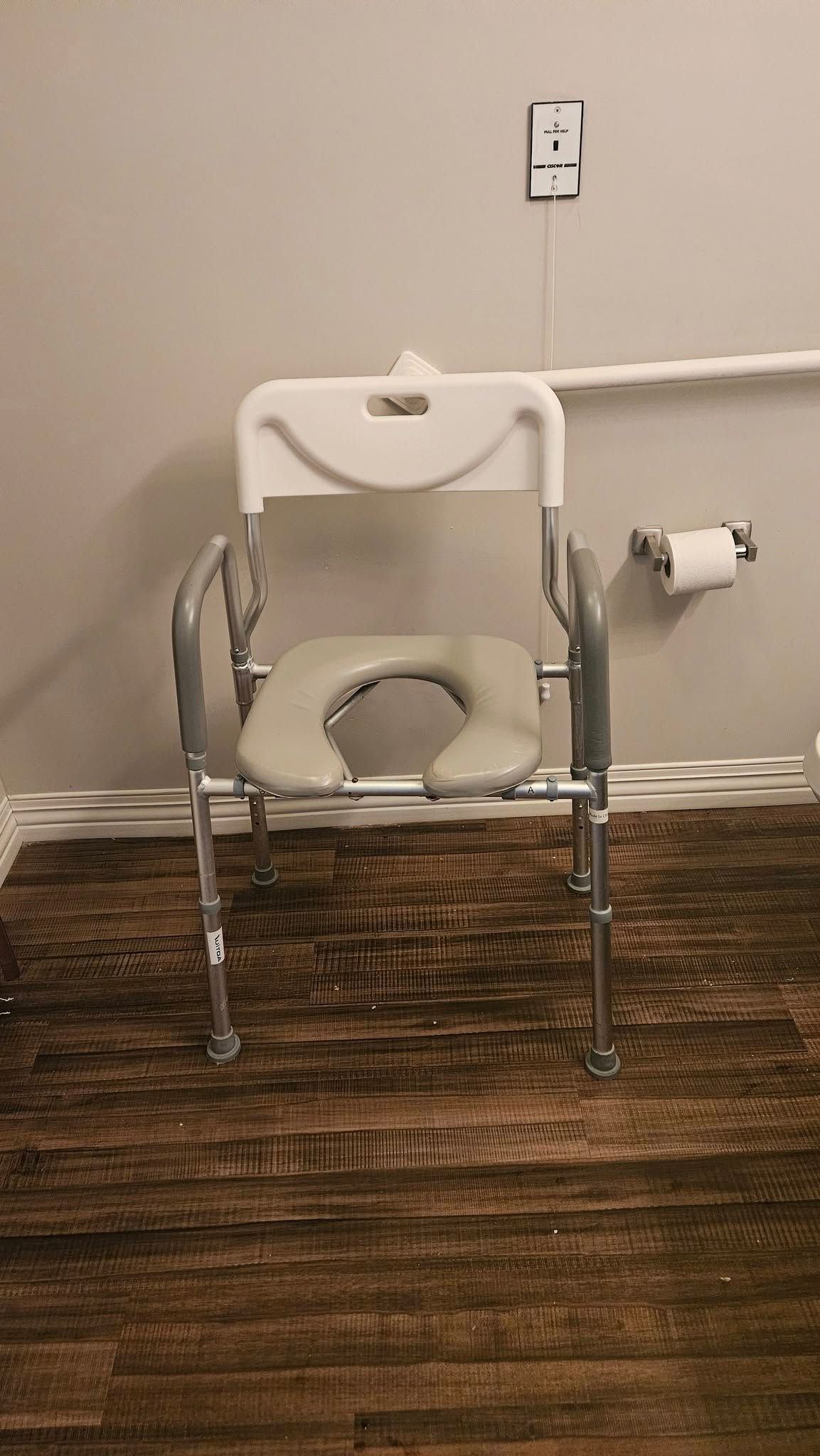A commode chair is sitting on a wooden floor in a bathroom.