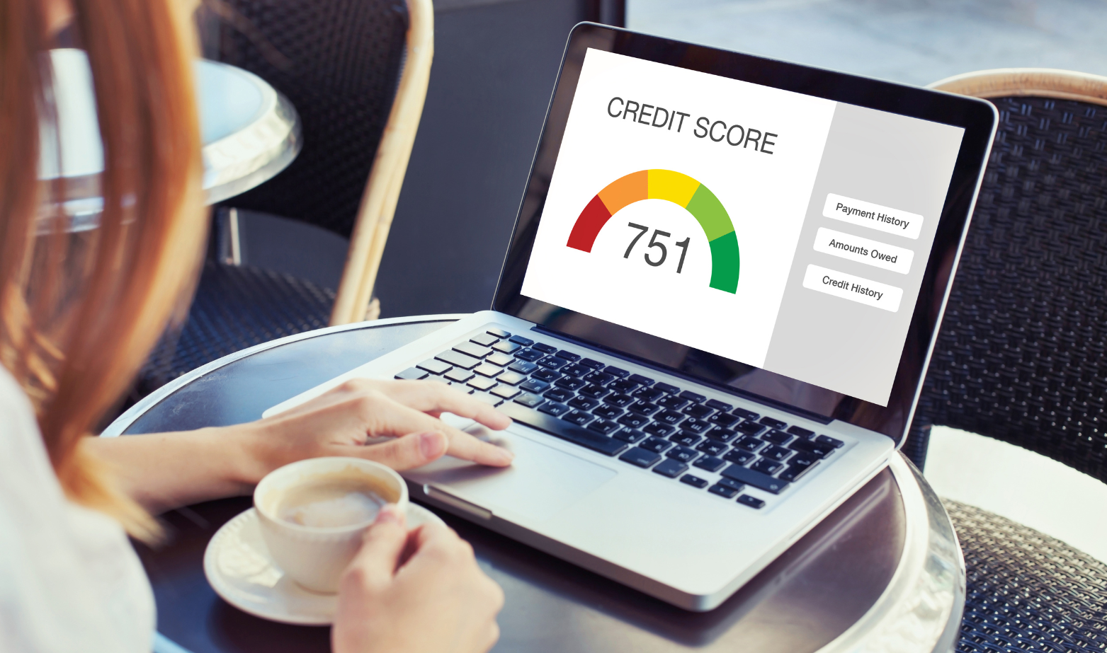 A woman is sitting at a table using a laptop computer with a credit score of 751.