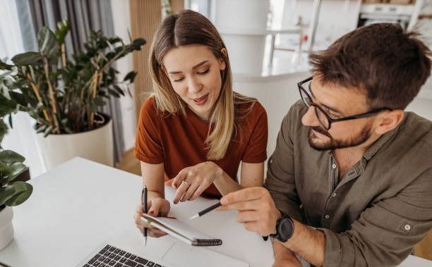 A man and a woman are sitting at a table looking at a tablet.