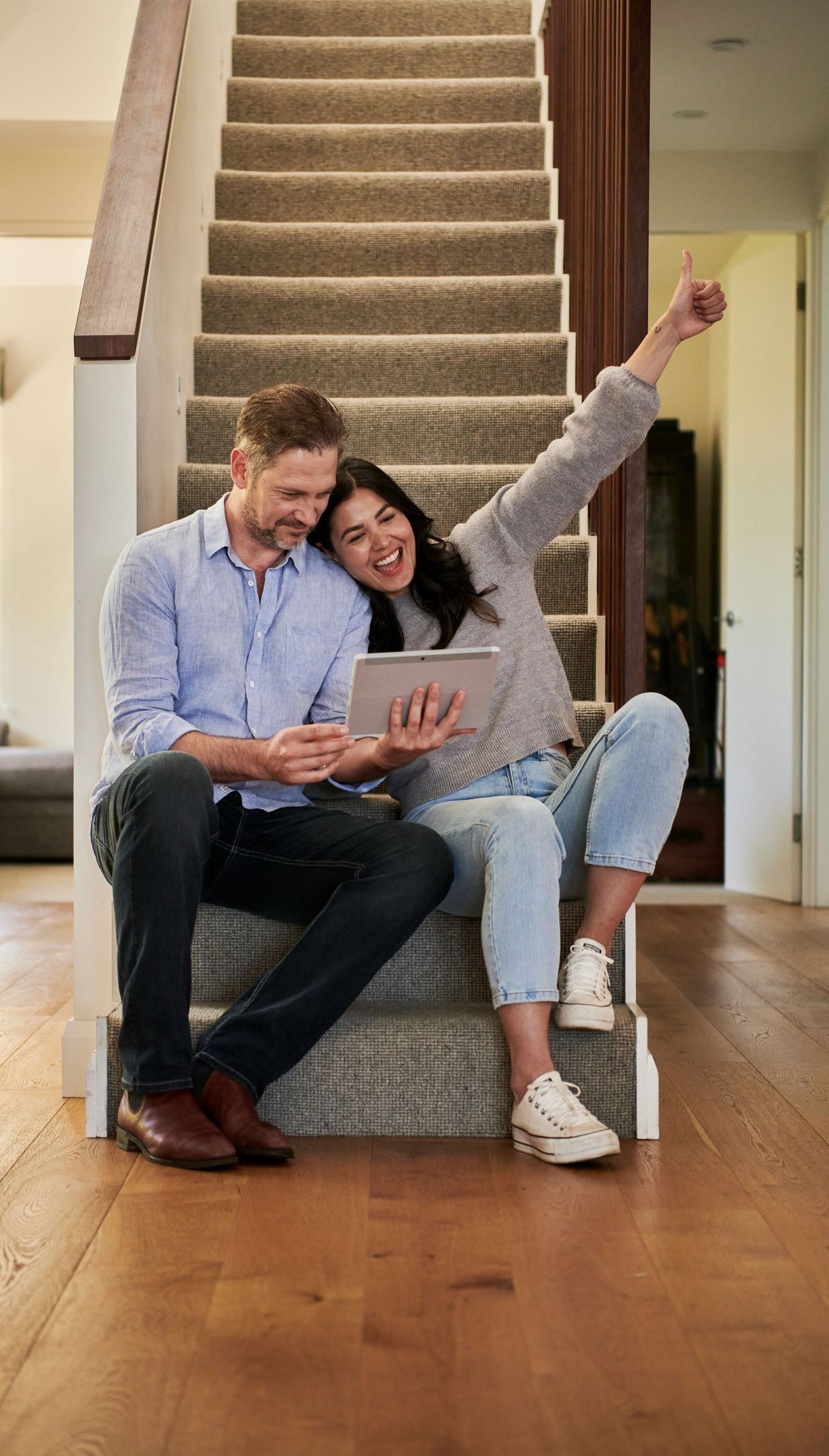 A man and a woman are sitting on the stairs looking at a tablet.