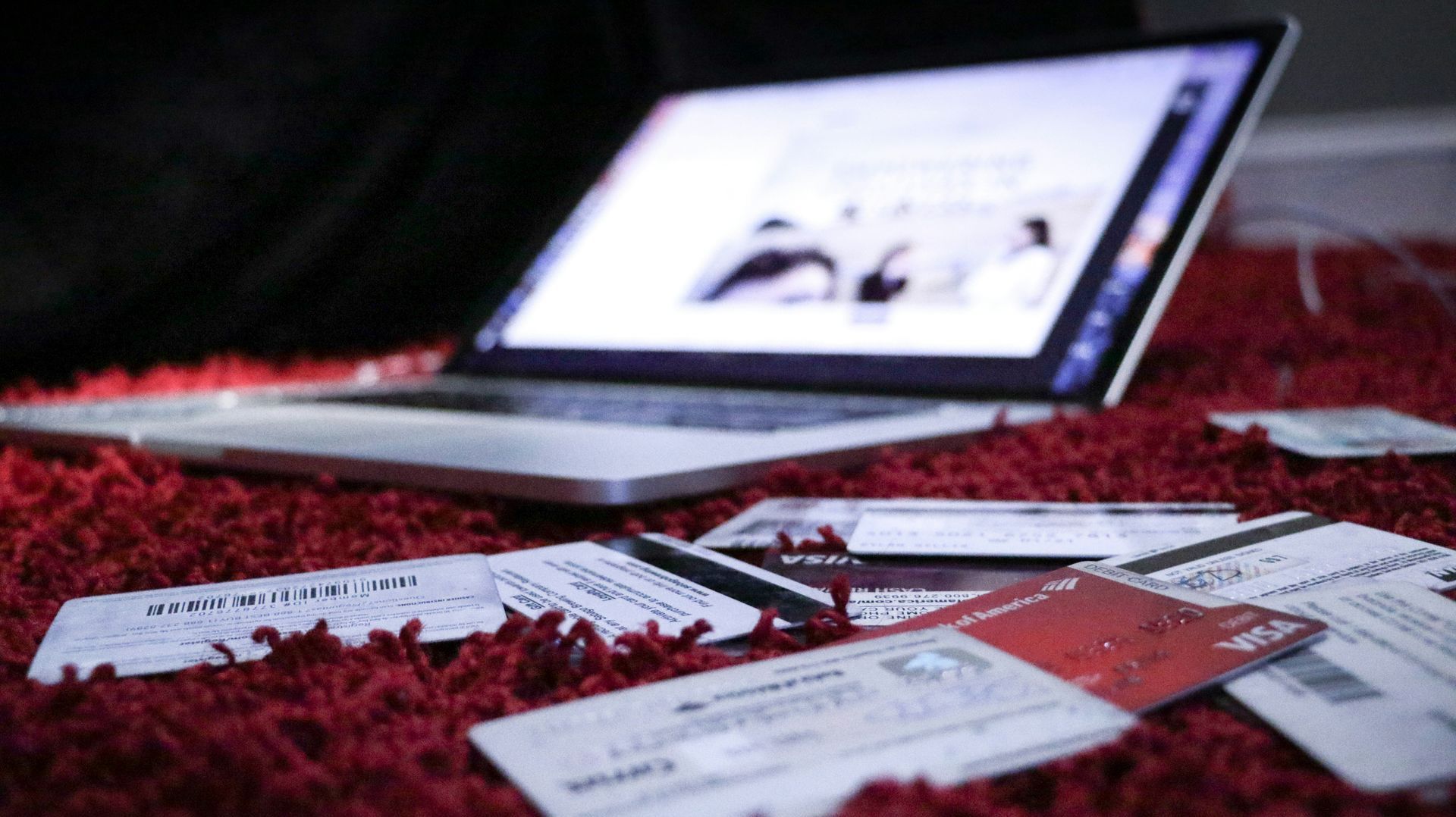 A laptop computer is sitting on a red rug next to credit cards.