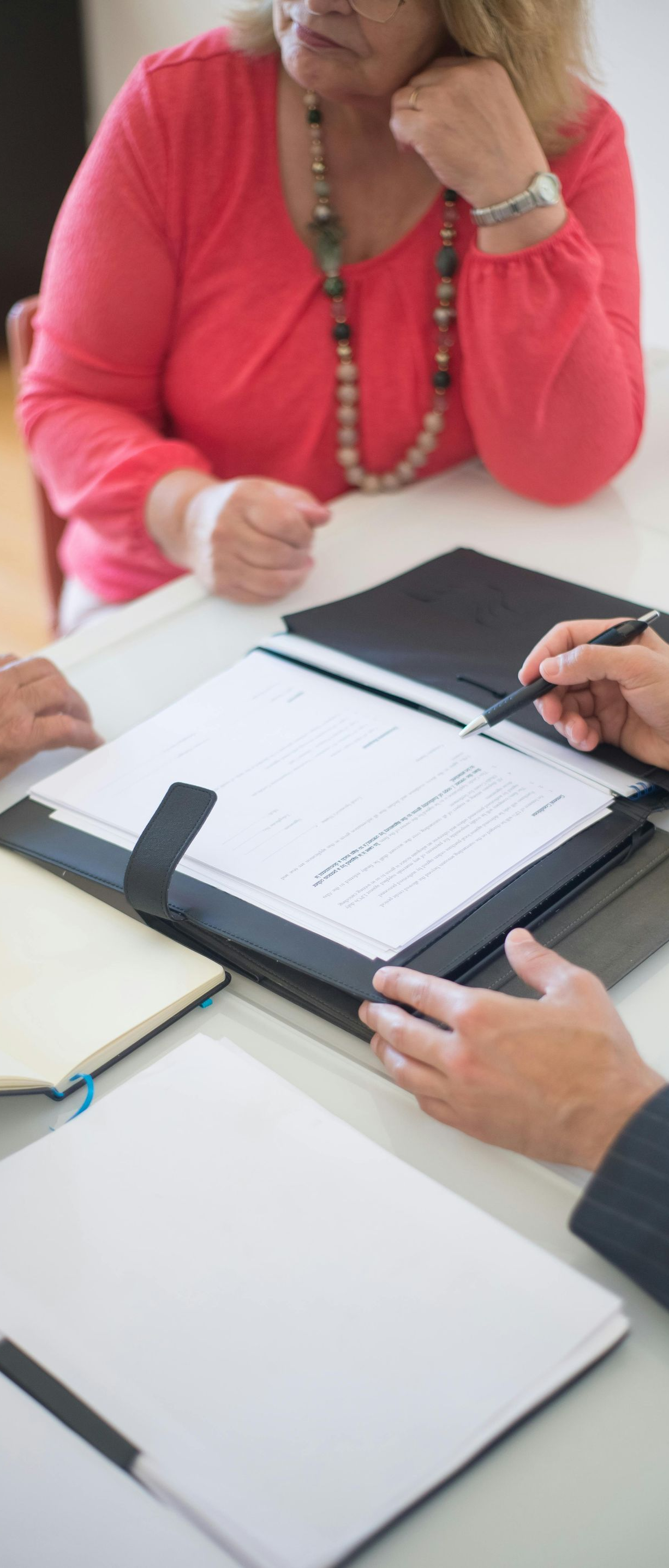 A woman in a red top reviews documents with two other people at a table.