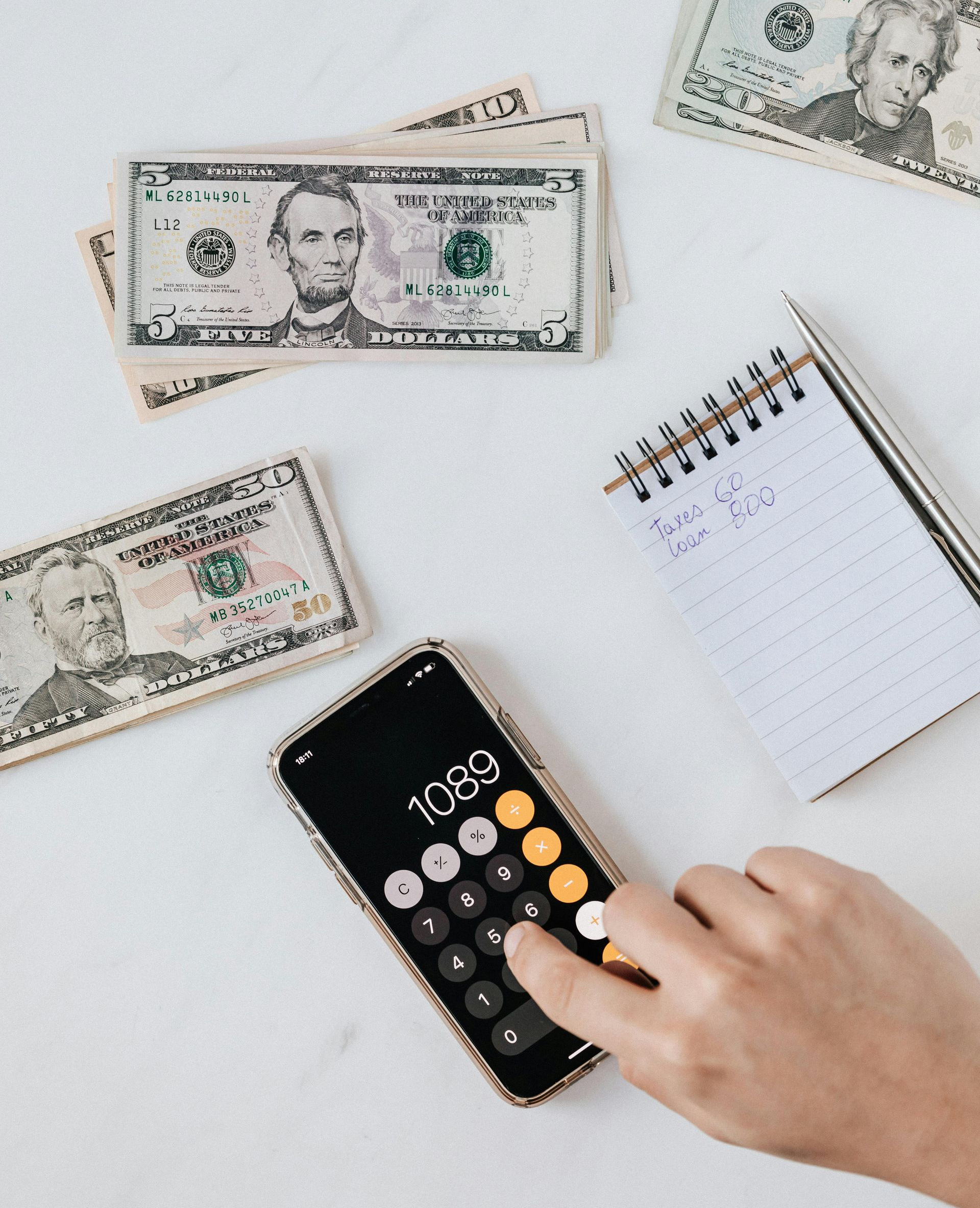 Hand using calculator next to money and notepad. Budgeting or financial planning concept.