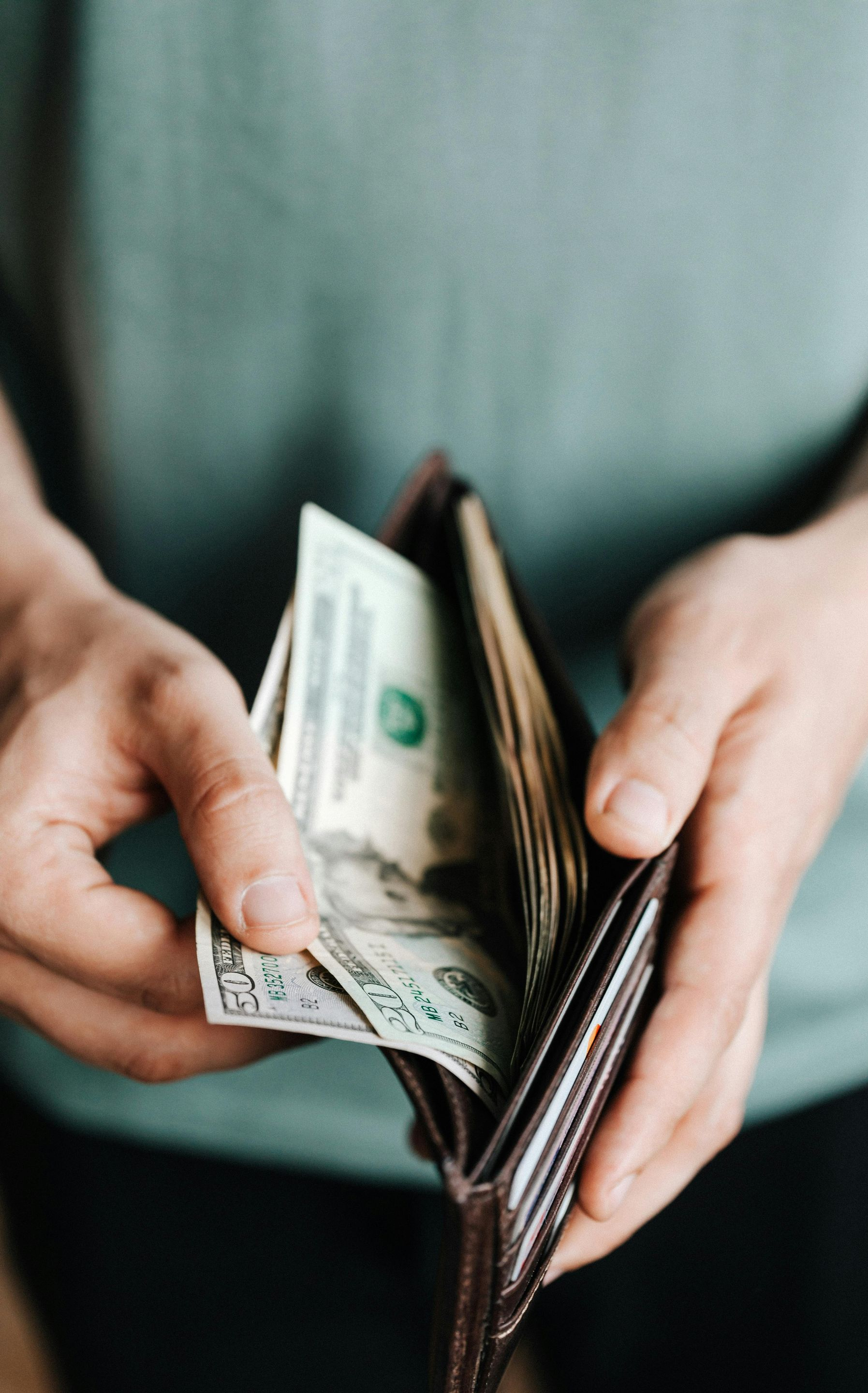 Person holding open brown wallet with money inside.