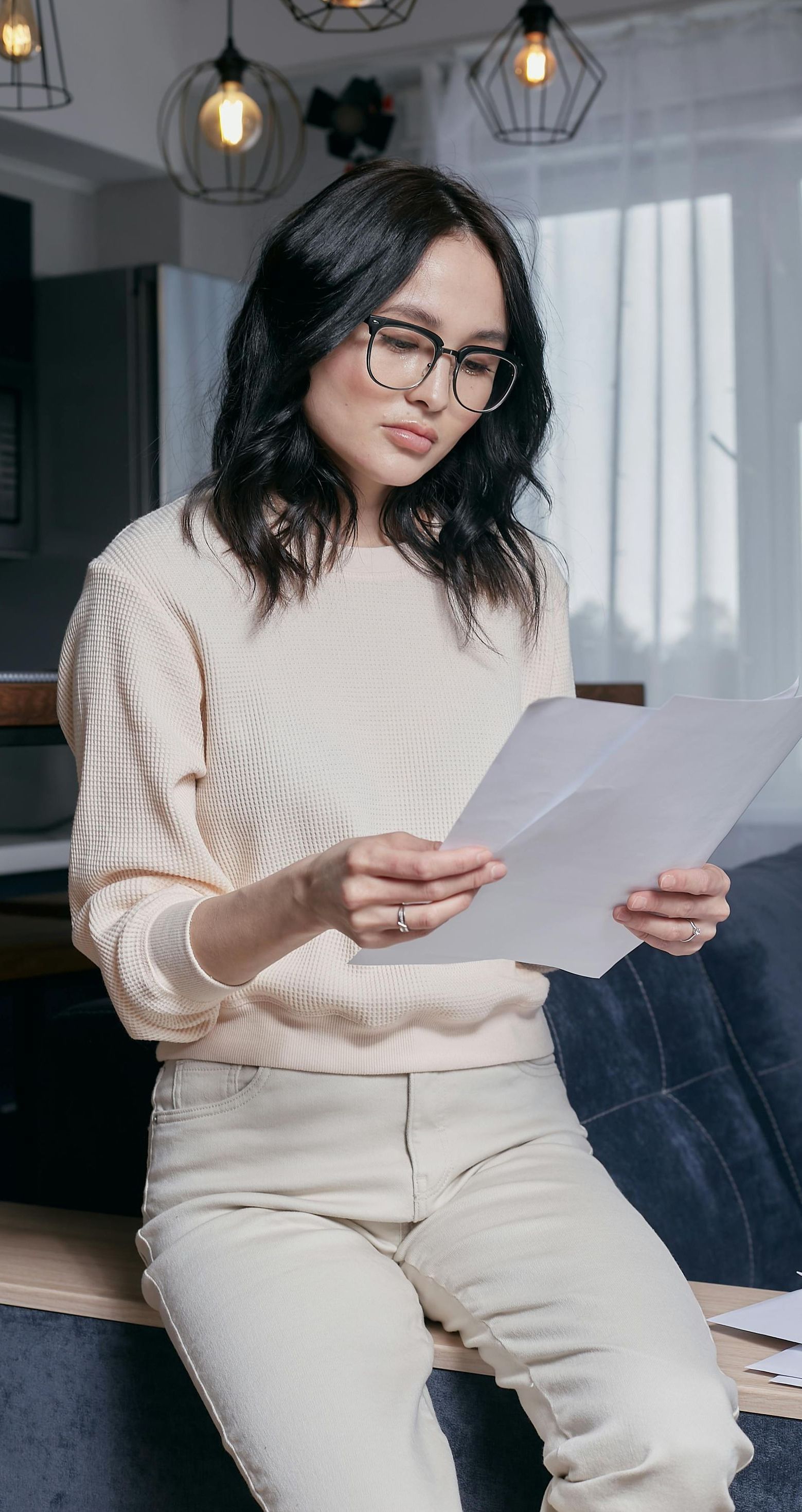 A woman is sitting on a couch reading a piece of paper.