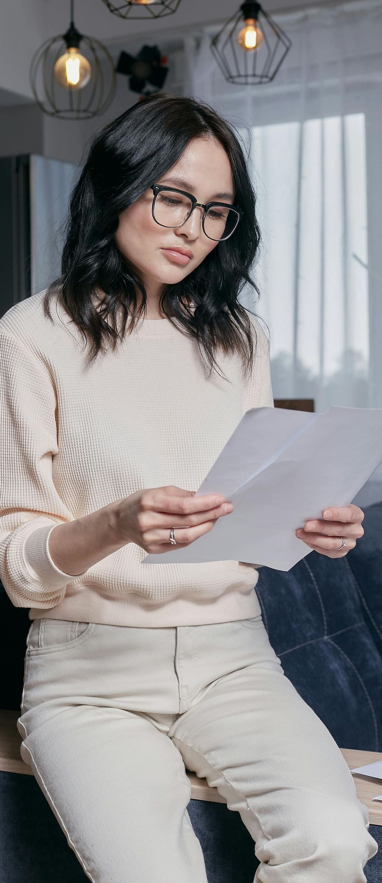 A woman is sitting on a couch reading a piece of paper.