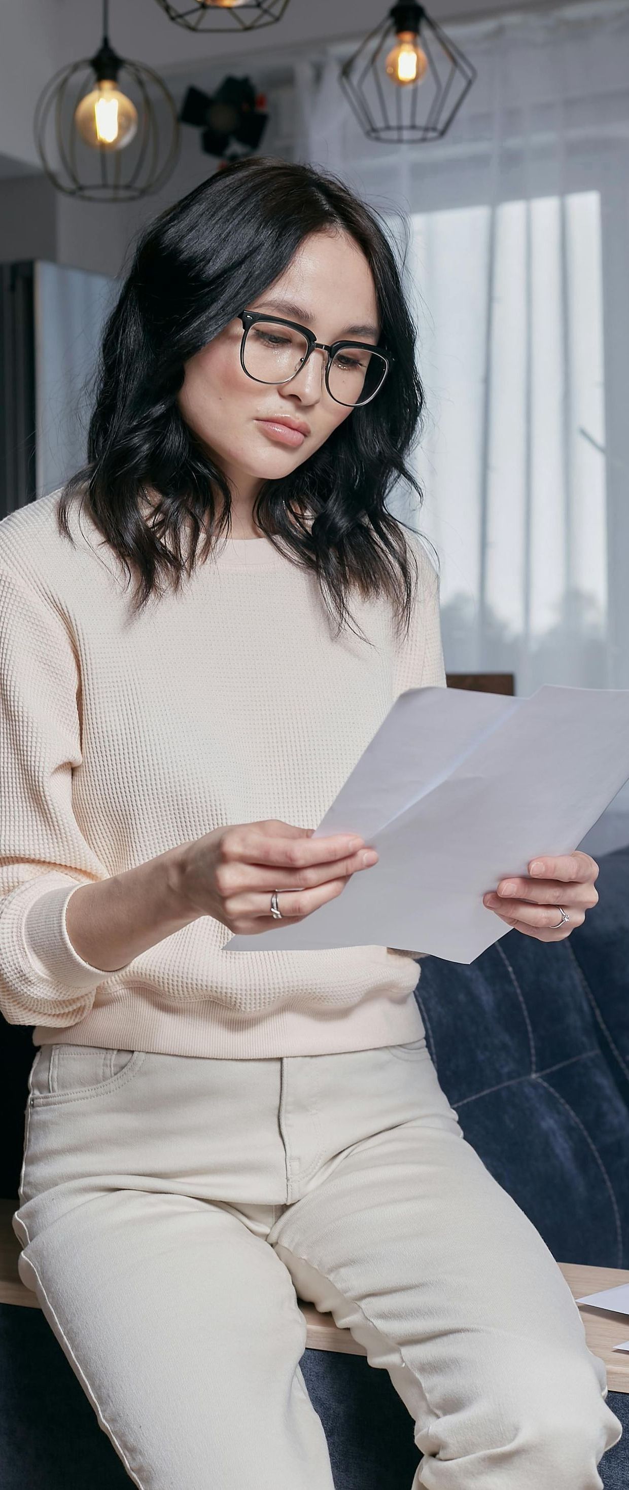 A woman is sitting on a couch reading a piece of paper.