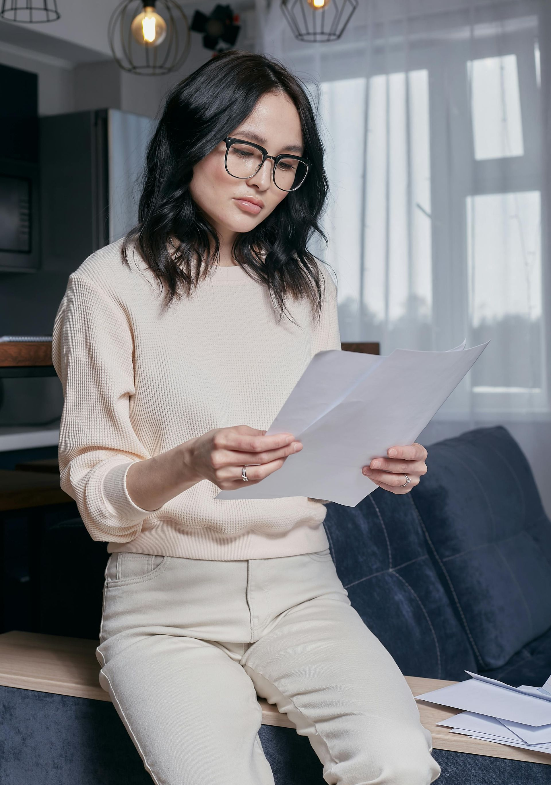 A woman is sitting on a couch reading a piece of paper.