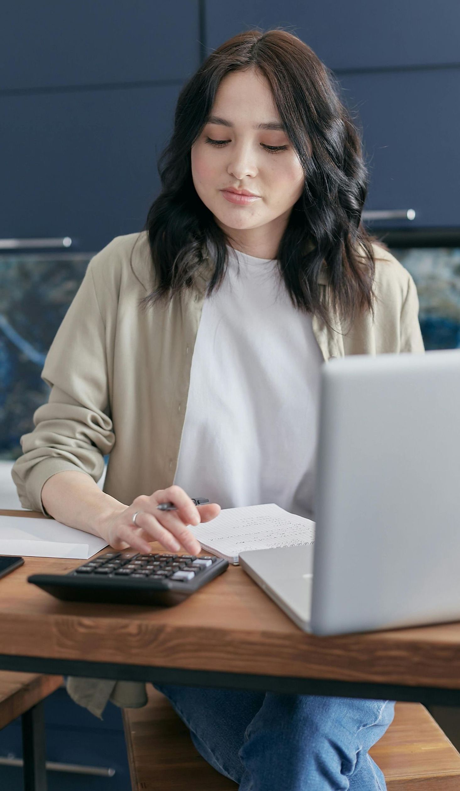 A woman is sitting at a table with a laptop and a calculator.