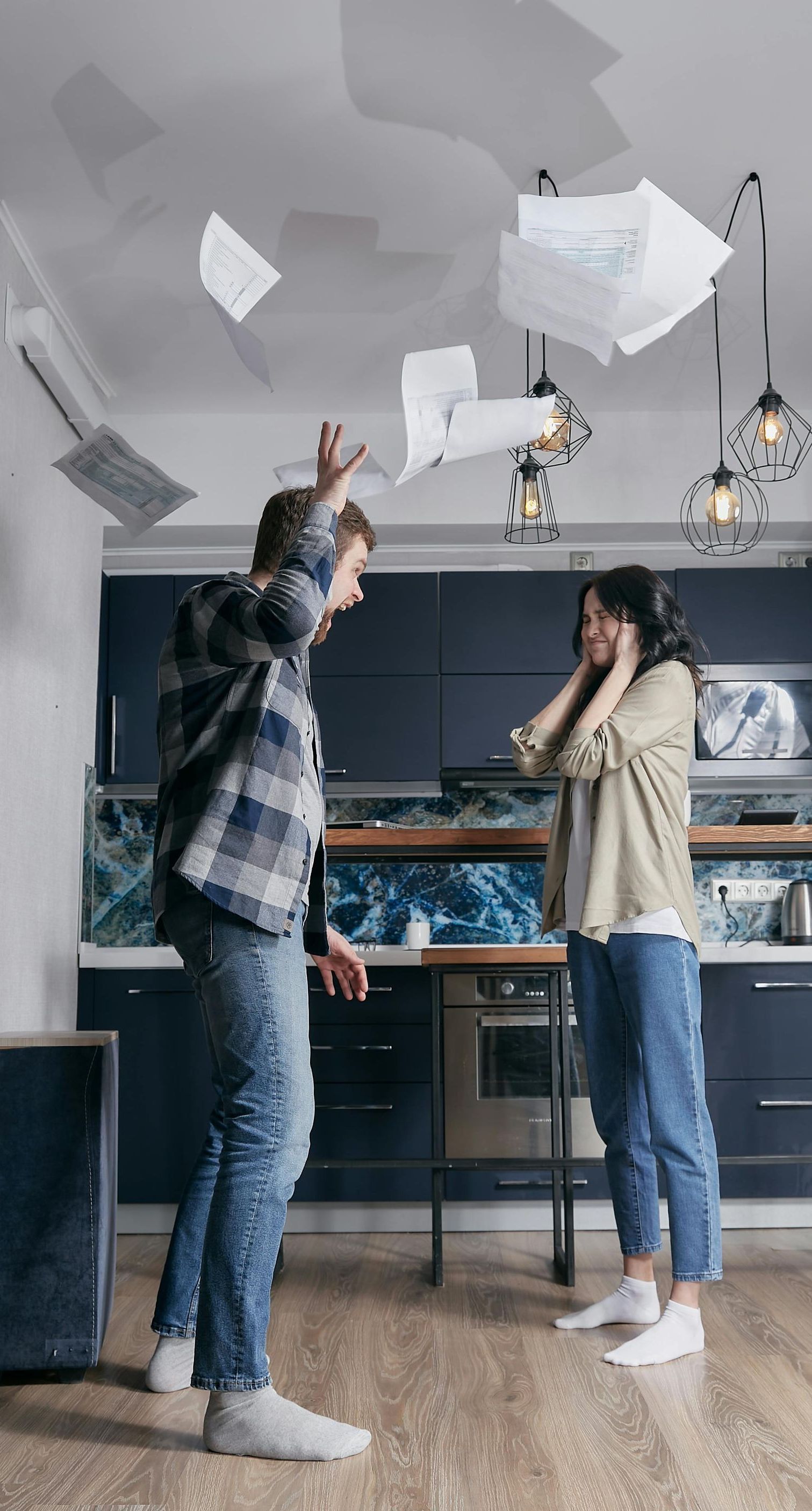 A man and a woman are throwing papers in the air in a kitchen.
