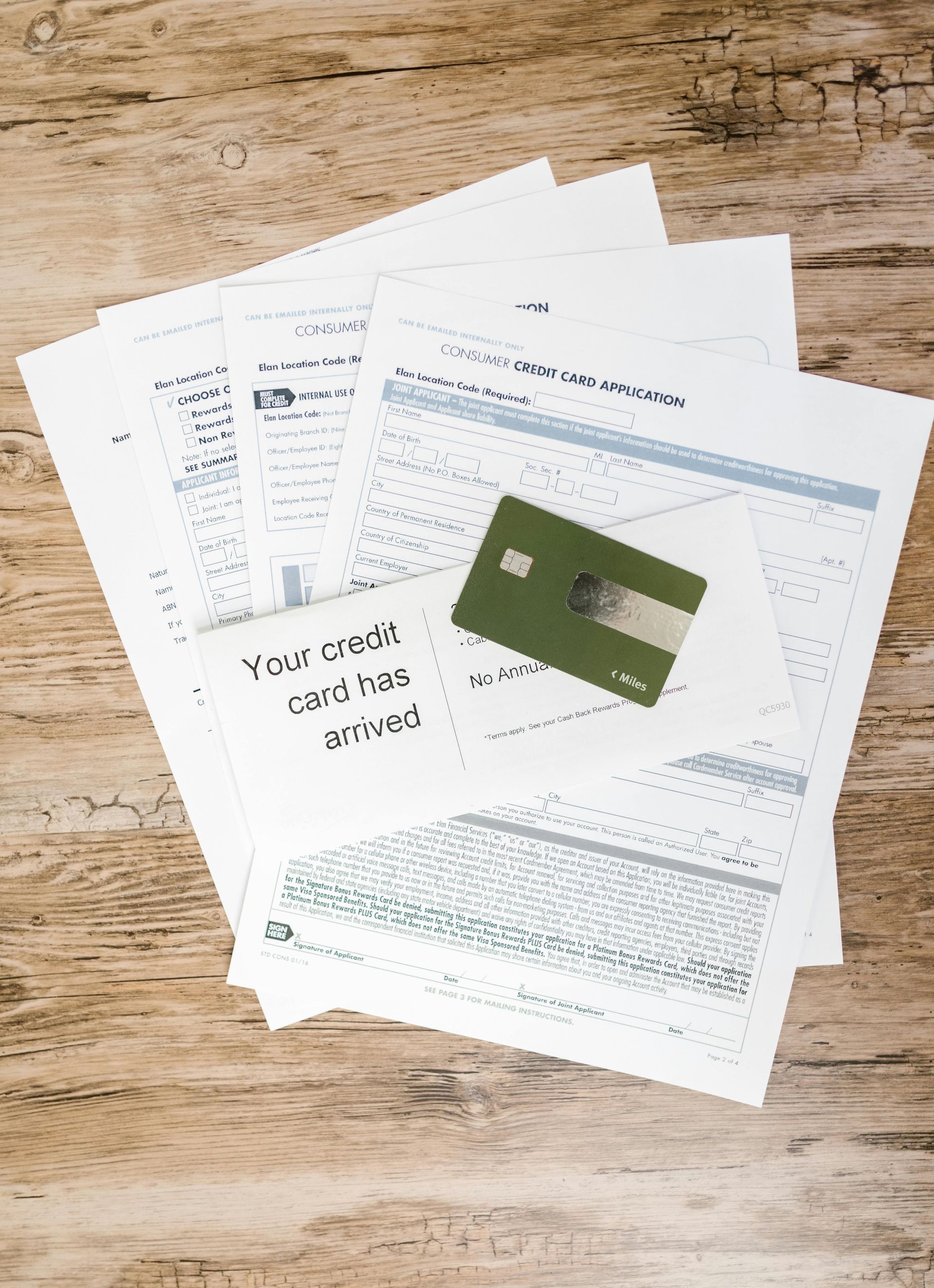 A stack of papers and a credit card on a wooden table.