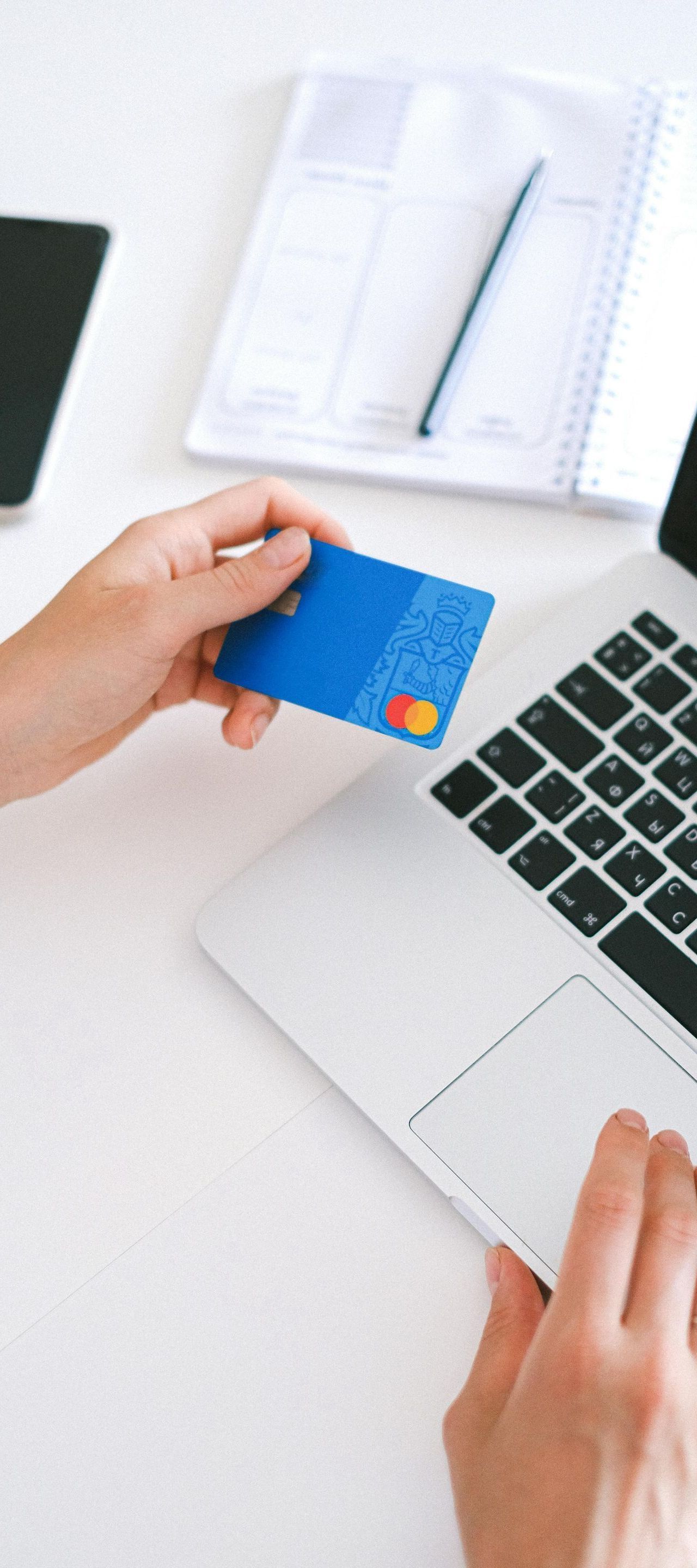 A person is holding a credit card in front of a laptop computer.