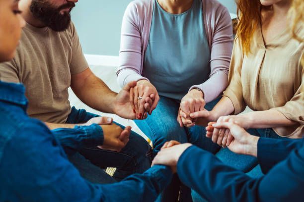 Close-up of hands of people sitting in a circle during a therapy group meeting.
