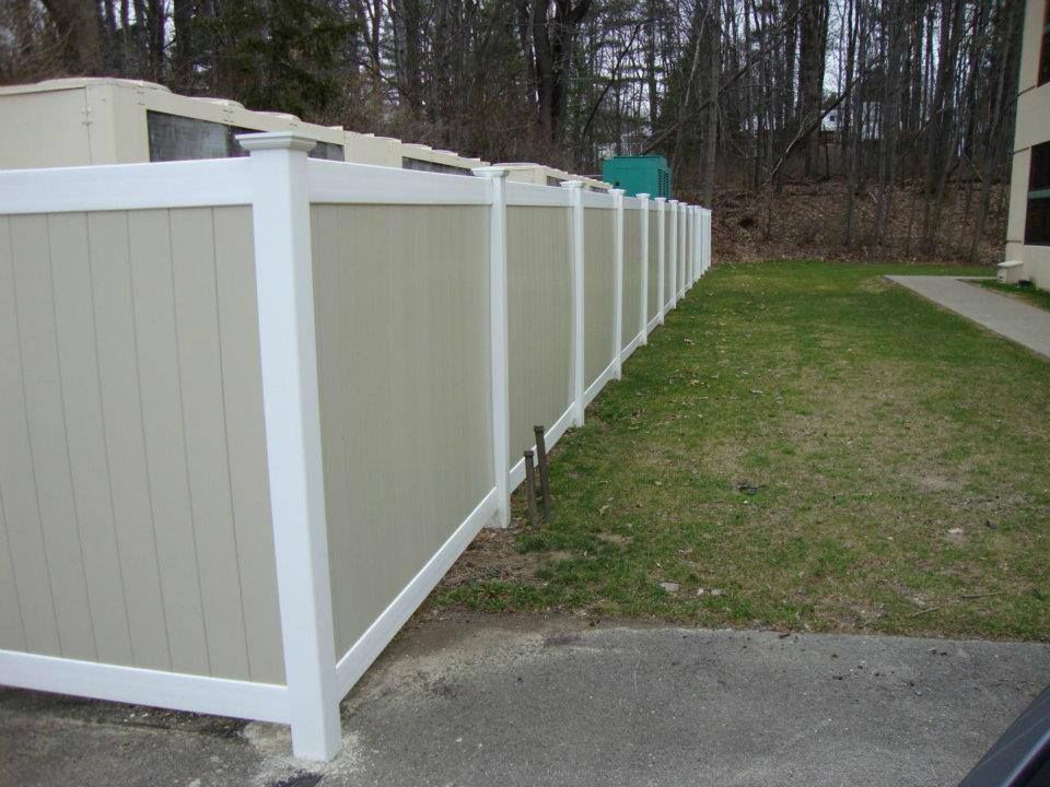 A white and tan fence surrounds a lush green yard