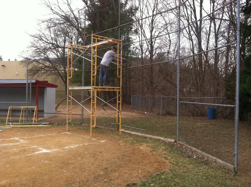 A man is standing on a scaffolding near a chain link fence