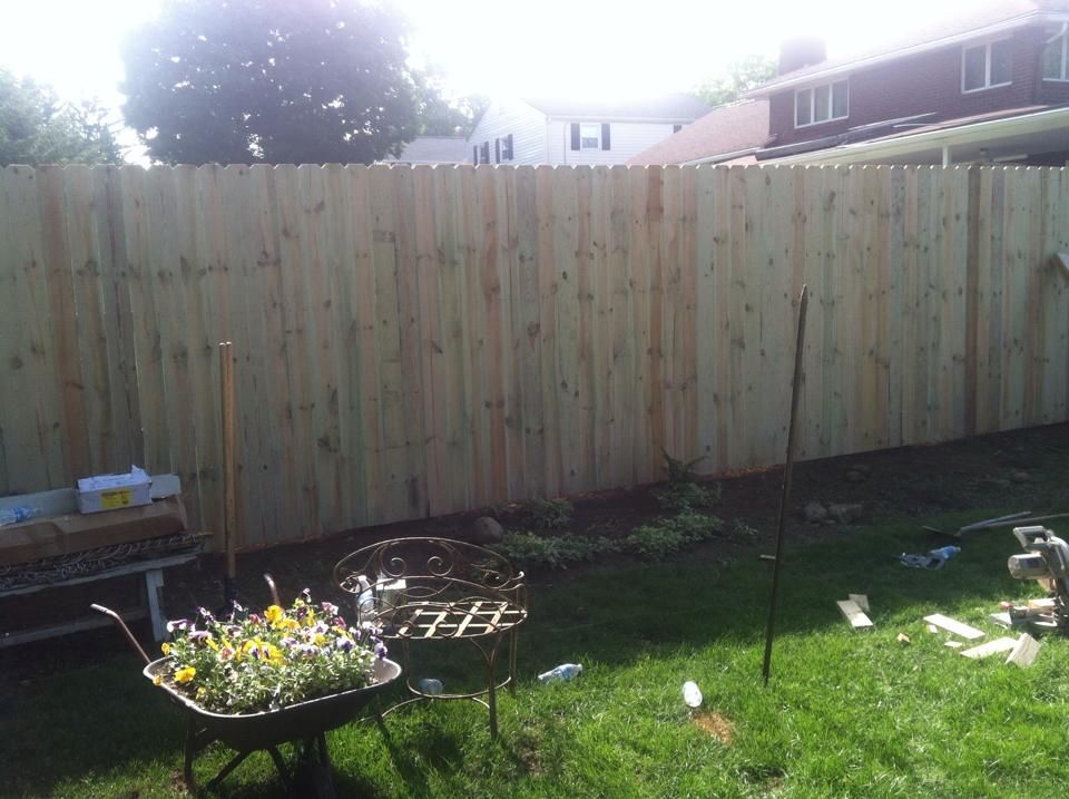 A wheelbarrow full of flowers sits in front of a wooden fence