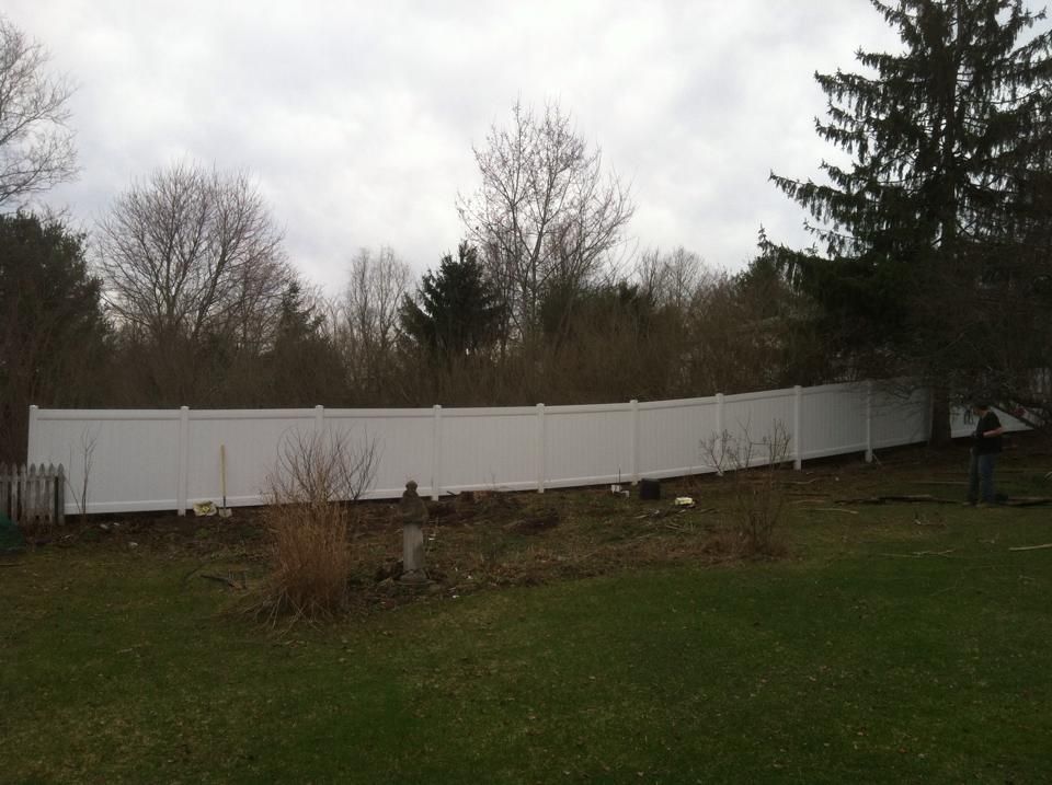 A white fence surrounds a grassy yard with trees in the background.