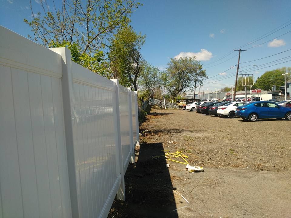 A white fence surrounds a parking lot with cars parked behind it
