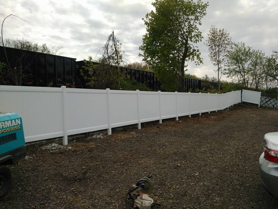 A white fence is sitting in a gravel lot next to a car.